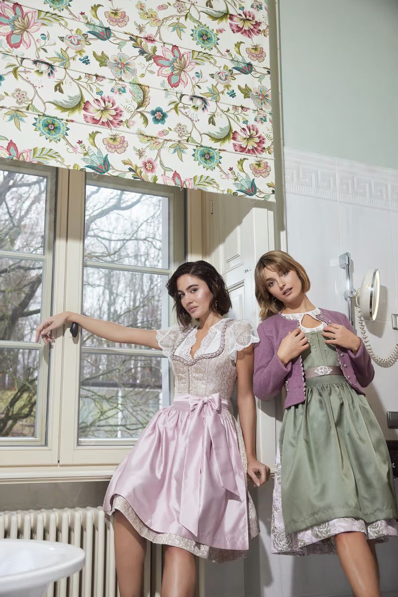 Women wearing Kruger Mini Dirndl dresses, one in pink with ornamental bodice and skirt, styled in a vintage setting.